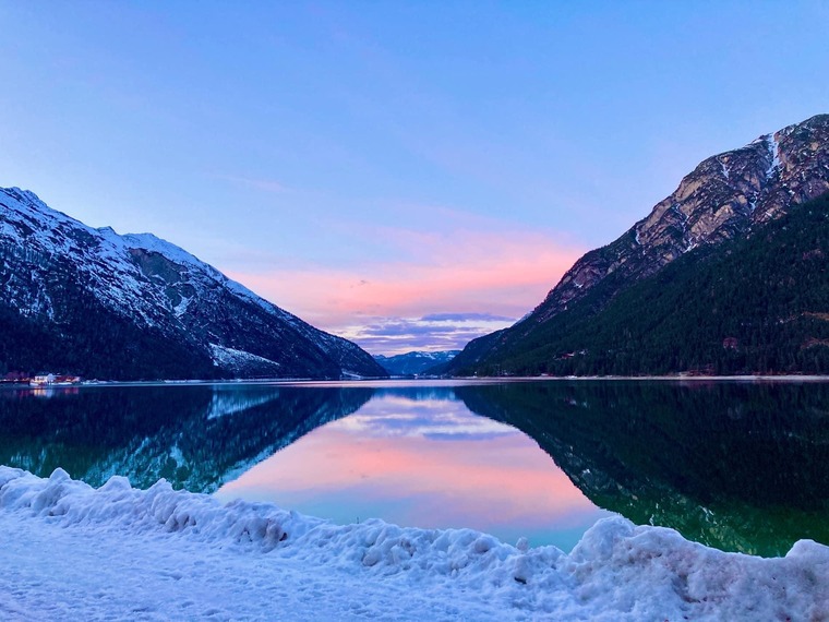 Winterurlaub in Österreich: Blick auf den Achensee im Winter, im Hintergrund schneebedeckte Berge und ein rosaroter Abendhimmel. 