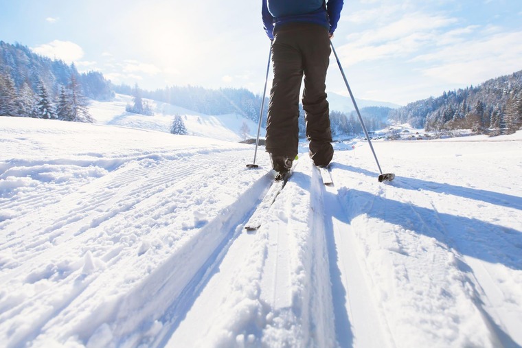 Winterurlaub in Österreich: Blick auf eine Langlaufloipe mit den Beinen eines Langläufers, im Hintergrund die Berge. 