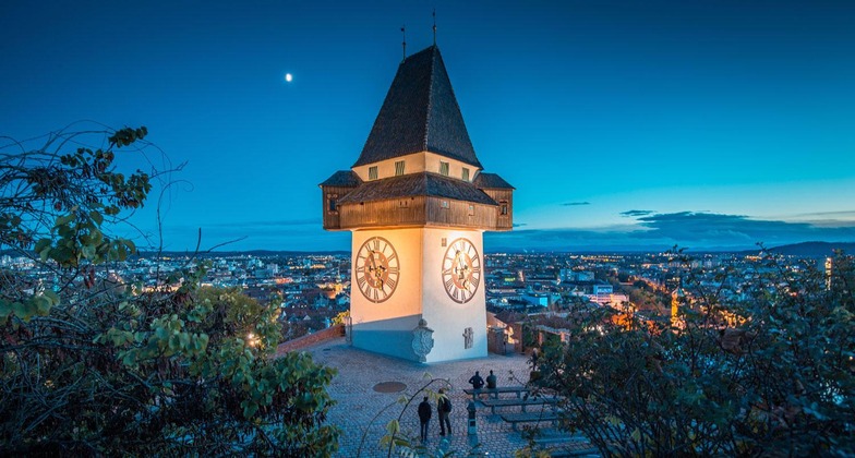 Graz Sehenswürdigkeiten: Blick auf den Grazer Uhrturm und die dahinterliegende Stadt bei Nacht. 