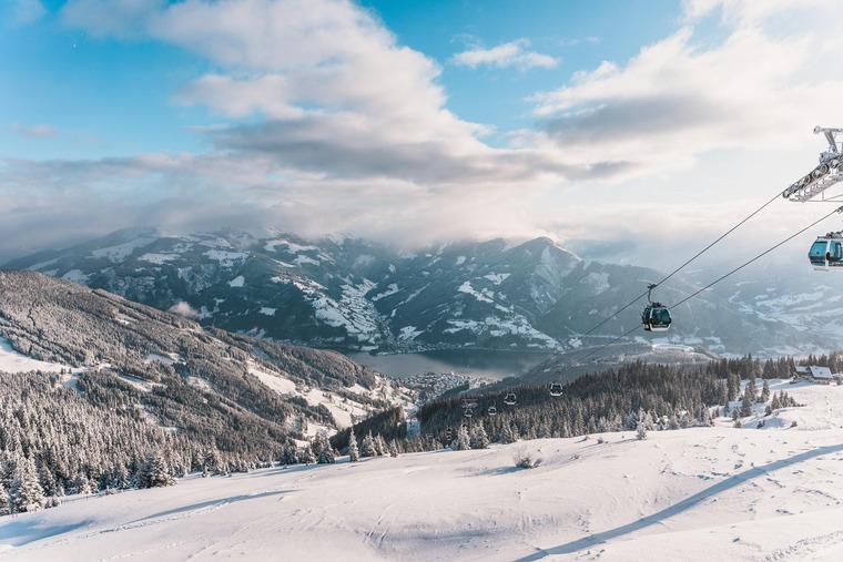 Skifahren in Österreich: Blick auf das Gletscherskigebiet Zell am See-Kaprun. Unter leicht bewölktem Himmel sieht man eine Piste, links im Bild eine Bergbahn. 