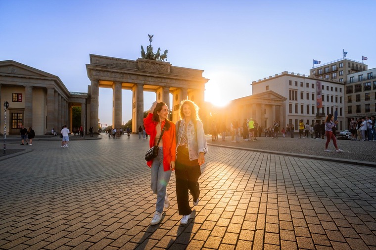 Die schönsten Städte Deutschlands: Zwei junge Frauen gehen vor dem Brandenburger Tor auf die Kamera zu. 