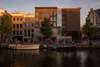 Zu den Sehenswürdigkeiten in Amsterdam zählt auf jeden Fall auch das Anne Frank Haus. Auf dem Bild sieht man das Haus von außen in der Abendsonne, der Blick von der anderen Seite einer Gracht. Davor liegen Boote im Wasser. 