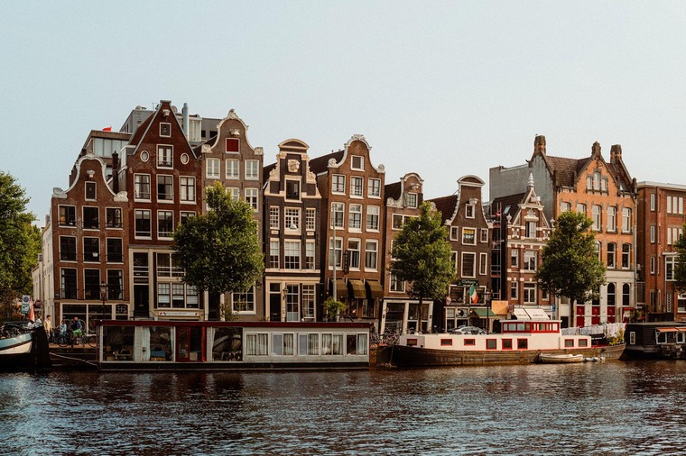 Zu den Sehenswürdigkeiten in Amsterdam gehört eine Grachtentour. Auf dem Bild zu sehen ist  Schiff mit Passagieren vor einem alten Gebäude.