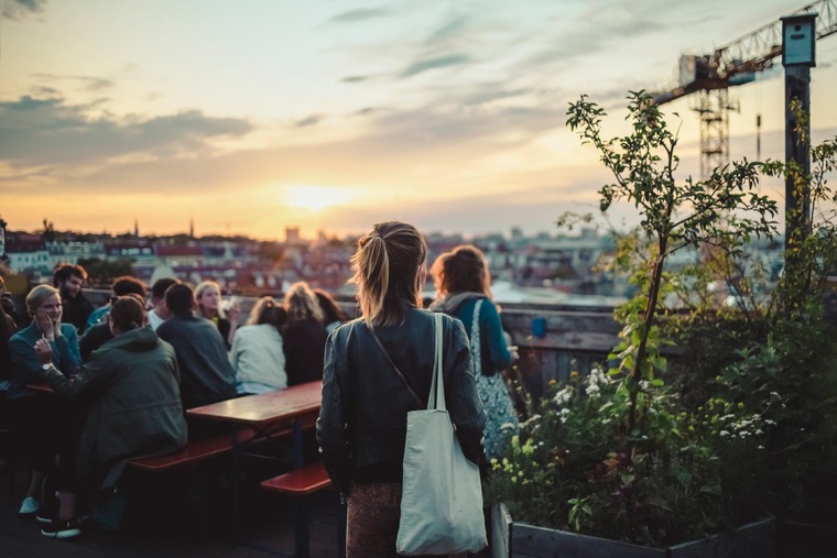 Sehenswürdigkeiten und Geheimtipps Berlin: Der Klunkerkranich sollte ein fixer Bestandteil jedes Berlin-Trips sein. Auf dem Bild sieht man eine junge Frau mit einem Rucksack, wie sie über das Berlin bei Sonnenuntergang blickt. 