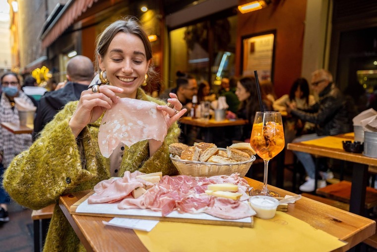 Zu den Bologna Sehenswürdigkeiten gehört die Kulinarik. Auf dem Bild sieht man eine Frau, die Mortadella isst.