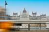 Budapest Sehenswürdgkeiten: Blick auf das Parlament in Budapest von der gegenüberliegenden Flussseite, davor sieht man unscharf eine Straßenbahn vorbei fahren. 