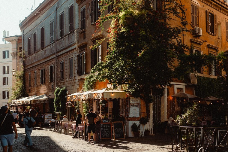 Trastevere ist eines der Viertel in Rom, das noch sehr lebendig ist. Bars, Restaurants, kleine Gässchen: Es ist definitiv ein Geheimtipp für Rom. Im Bild sieht man eine alternde, mit Grün bewachsene Häuserecke, links und rechts Kopfsteinpflastergassen, alles im Licht der Abendsonne. 