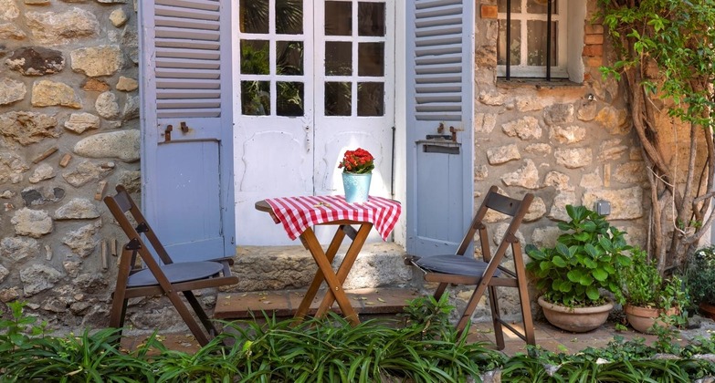 Sehenswürdigkeiten an der Cote d'Azur: Blick auf typisches Bild in Antibes. Ein kleiner Holztisch, links und rechts mit einem Klappstuhl aus Holz, stehen vor einer Glastüre eines alten Hauses. 