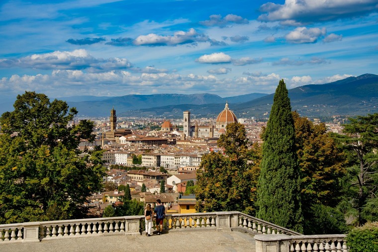 Zu den top Florenz Sehenswürdigkeiten gehört der Piazzale Michelangelo. Auf dem Bild sieht man zwei Personen, wie sie die Aussicht auf die Stadt an einem Sommertag genießen.