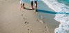 Mit dem Zug zum Urlaub am Meer: Mutter und Kind gehen am Strand spazieren, im Sand sieht man ihre Fußspuren. 