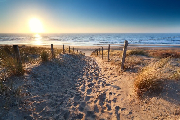 Mit dem Zug zum Urlaub am Meer: Blick auf den weißen Sandstrand in Zandvoort in Holland, darüber der blaue Himmel. 