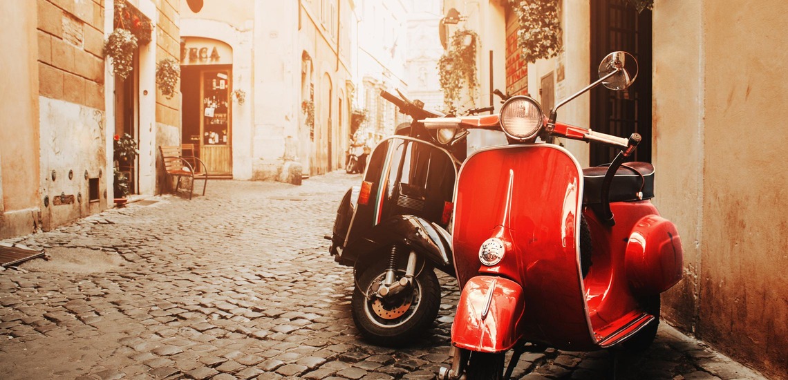 Geheimtipps Rom: Eine Gasse im sanften Licht, im Vordergrund sieht man eine rote Vespa. 