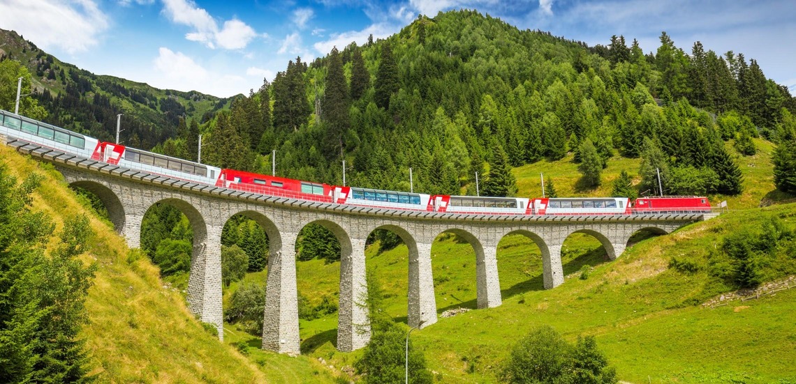 Glacier Express: Bild des Zuges auf der Strecke in grüner Sommerlandschaft. 