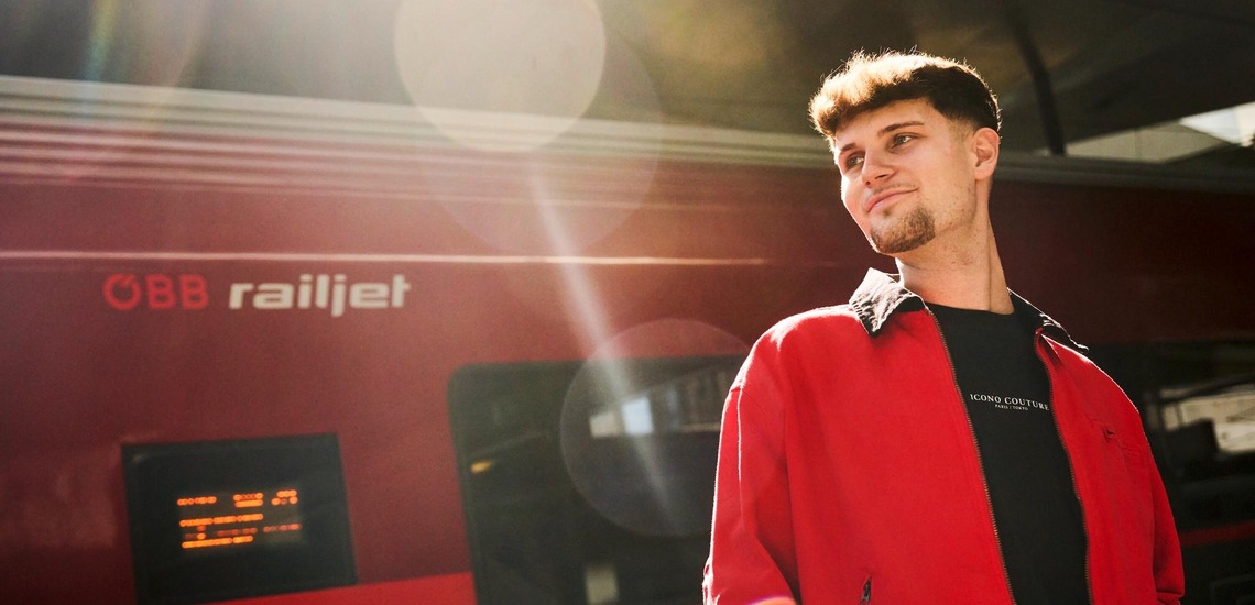 Günstig reisen: Ein junger Mann steht vor einem Railjet und blickt in die Ferne. 
