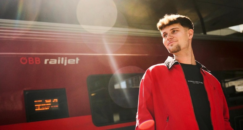 Günstig reisen: Ein junger Mann steht vor einem Railjet und blickt in die Ferne. 