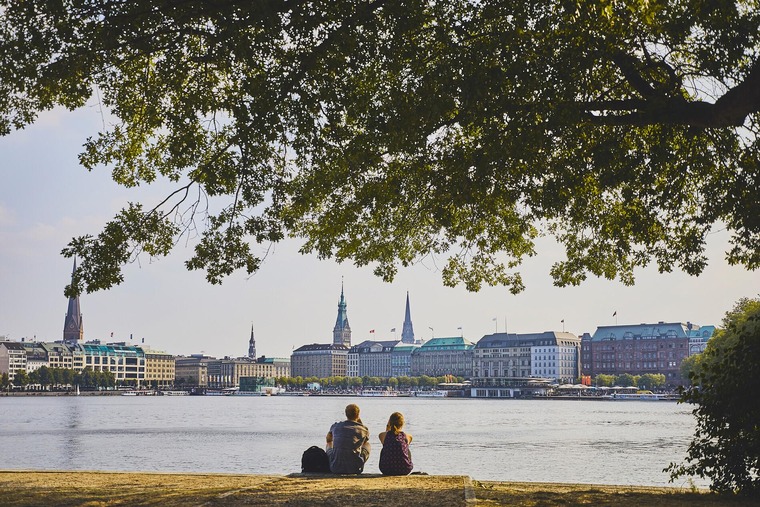 Hamburg Highlights: Zwei Menschen sitzen am Flussufer und Blicken auf die Stadt