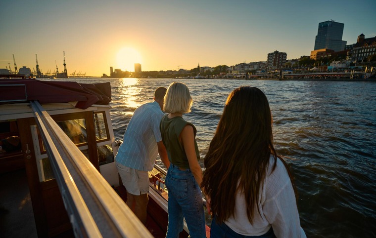 Hamburg Highlights: Drei junge Menschen stehen bei Sonnenuntergang am Hamburger Hafen und blicken in Richtung Meer