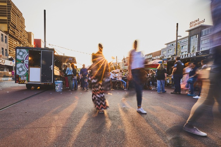 Hamburg Highlights: Der Spielbudenplatz mit dem Nachtmarkt St. Pauli. Die untergehende Sonne scheint zwischen Menschen durch, die sich zwischen Marktständen am Platz bewegen. 