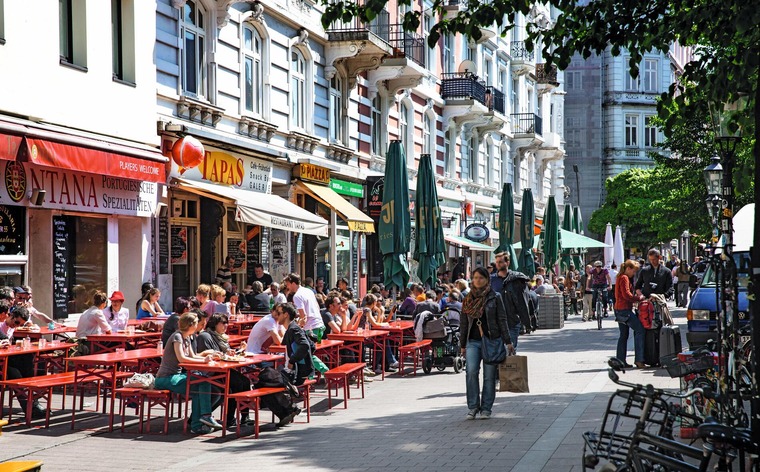 Hamburg Highlights: Ein Blick auf eine belebte Straße im Schanzenviertel, Menschen sitzen in Gastgärten in der Sonne