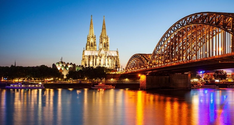 Sehenswürdigkeiten in Köln: Der Kölner Dom und die Hohenzollerbrücke glänzen im Wasser des Rheins bei Nacht. 