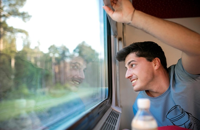 Mit dem Zug nach London: Auf dem Bild sieht man einen jungen Mann, der aus dem Fenster eines Zuges schaut.
