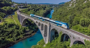 Nachhaltig reisen: Wunderschöne Zugstrecke in Slowenien. Ein Zug fährt über eine Brücke in einer sommerlichen Landschaft. 