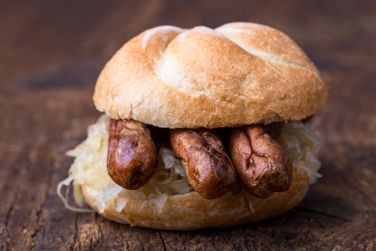 Sehenswürdigkeiten von Nürnberg für den Gaumen: Drei Nürnberger Rostbratwürste mit Sauerkraut in einer Semmel.