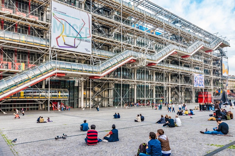 Zu den Sehenswürdigkeiten von Paris gehört das Centre Pompidou. Im Bild sieht man Menschen, die vor dem Gebäude auf den Stufen sitzen. 