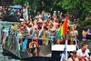 Top Pride Events Europa: Man sieht ein Boot in einer Gracht von Amsterdam mit feiernden Menschen, die in Regenbogenfarben gekleidet sind. 