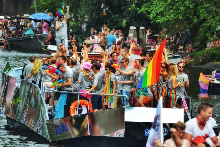 Top Pride Events Europa: Man sieht ein Boot in einer Gracht von Amsterdam mit feiernden Menschen, die in Regenbogenfarben gekleidet sind. 