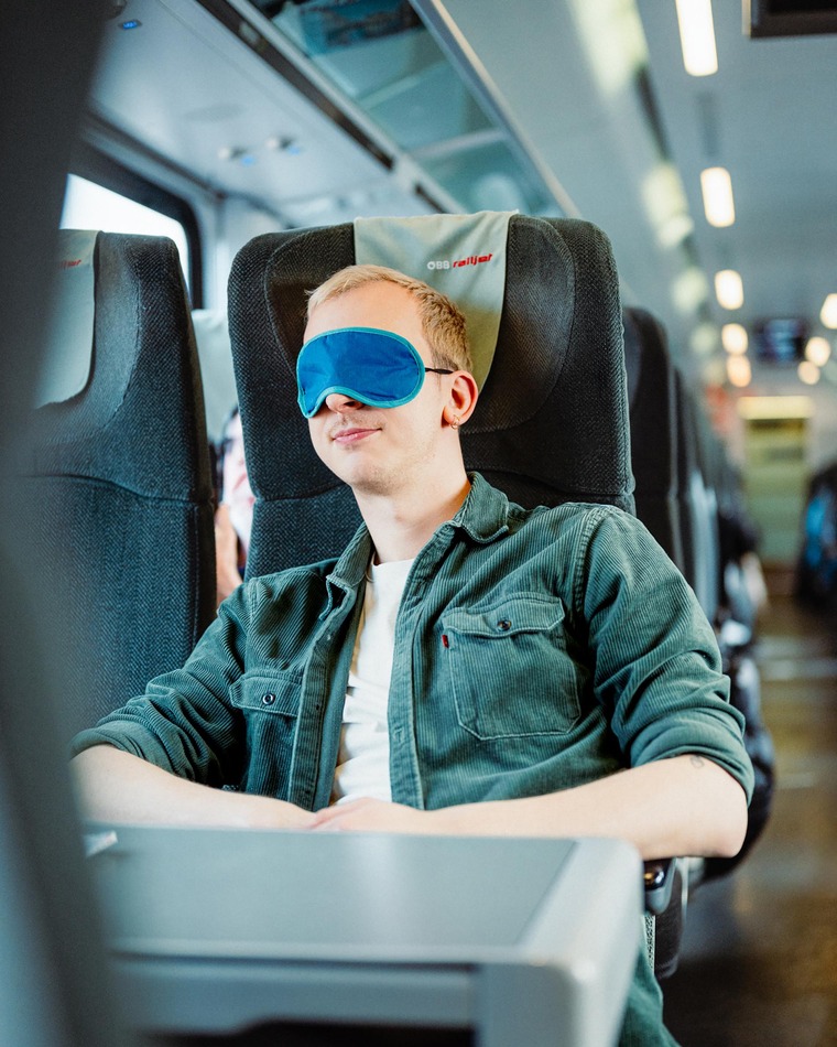 Smart Reisen - entspannter junger Mann mit Schlafmaske im Railjet