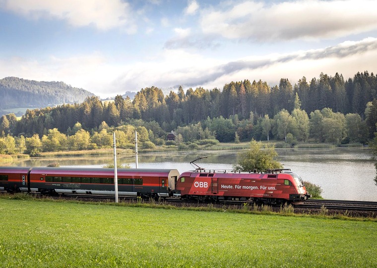 Reise planen: Unser Tipp ist es, die Anreise schon als Teil der Urlaubs zu genießen. Im Bild sieht man einen Railjet, der in grüner Landschaft fährt. 