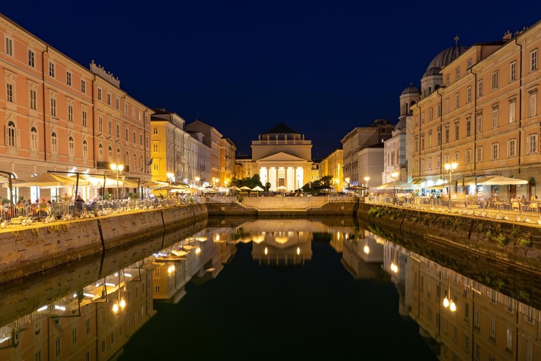 Triest Sehenswürdigkeiten: Blick auf den Canal Grande di Triest bei Nacht, wo sich die Lichter der belebten Lokale und Straßen im Wasser spiegeln. 