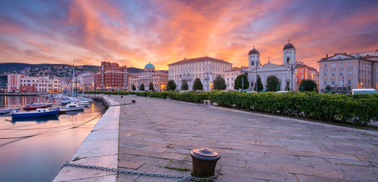 Triest Sehenswürdigkeiten: Ein Blick auf den Hafen und die Altstadt von Triest in der rot schimmernden Morgensonne. 