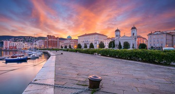 Triest Sehenswürdigkeiten: Ein Blick auf den Hafen und die Altstadt von Triest in der rot schimmernden Morgensonne. 