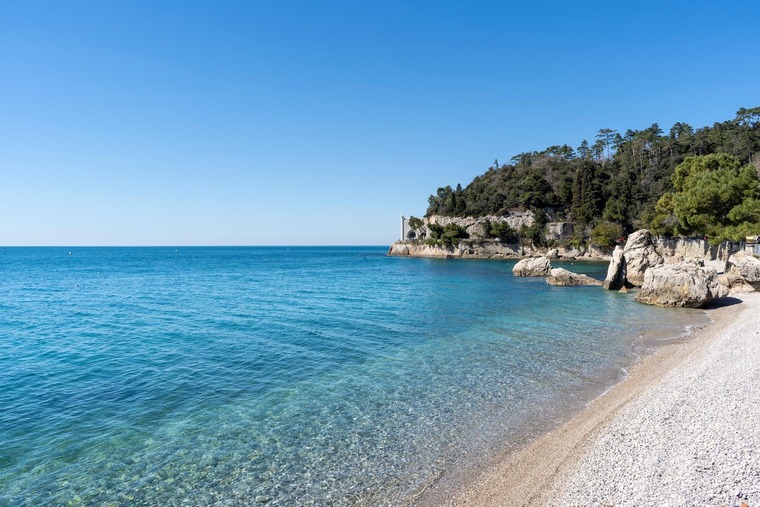 Triest Sehenswürdigkeiten: Der Strand Grignano, ganz in der Nähe des Schlosses Miramare, unter blauem Himmel und bei Sonnenschein. 