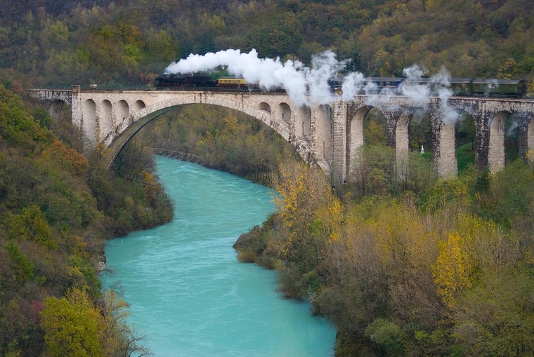 Zu einem Urlaub in Slowenien gehört die Wocheiner Bahn. Auf dem Bild sieht man den historischen Dampfzug, der über eine der alten Brücken fährt. 