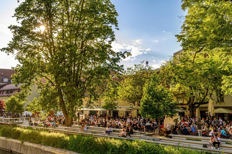 Zu einem Urlaub in Slowenien gehört auch ein Zwischenstopp in Ljubljana. Auf dem Bild sieht man die gut besuchte Uferpromenade der Stadt. 