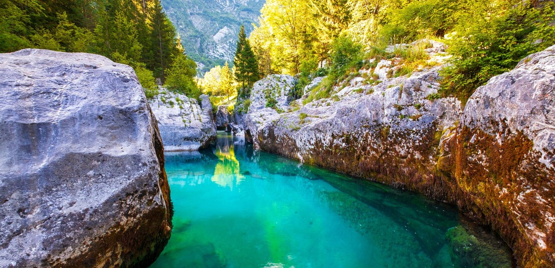 Ein Muss beim Urlaub in Slowenien ist ein Zwischenstopp im Soča-Tal. Auf dem Bild sieht man den smaragdgrünen Fluss, dahinter einen Blick auf die Berge. 