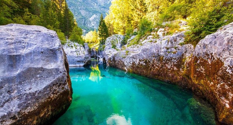 Ein Muss beim Urlaub in Slowenien ist ein Zwischenstopp im Soča-Tal. Auf dem Bild sieht man den smaragdgrünen Fluss, dahinter einen Blick auf die Berge. 