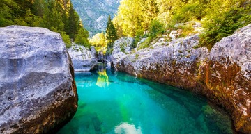 Ein Muss beim Urlaub in Slowenien ist ein Zwischenstopp im Soča-Tal. Auf dem Bild sieht man den smaragdgrünen Fluss, dahinter einen Blick auf die Berge. 