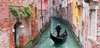 Venedig Sehenswürdigkeiten: Ein Gondolieri auf seiner Gondola in einem engen Kanal, gesäumt von bunten Häusern. 
