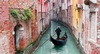 Venedig Sehenswürdigkeiten: Ein Gondolieri auf seiner Gondola in einem engen Kanal, gesäumt von bunten Häusern. 