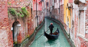Venedig Sehenswürdigkeiten: Ein Gondolieri auf seiner Gondola in einem engen Kanal, gesäumt von bunten Häusern. 