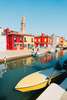 Venedig Sehenswürdigkeiten: Bunt gestrichene Häuser auf der Insel Burano, die man über einen Kanal hinweg sieht. Im Vordergrund dümpeln Gondolas im Wasser. 