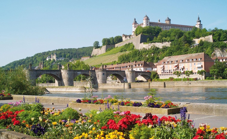 Zu den Sehenswürdigkeiten in Würzburg gehört die Festung Marienberg. Auf dem Bild sieht man sie vor dem Main-Kai.