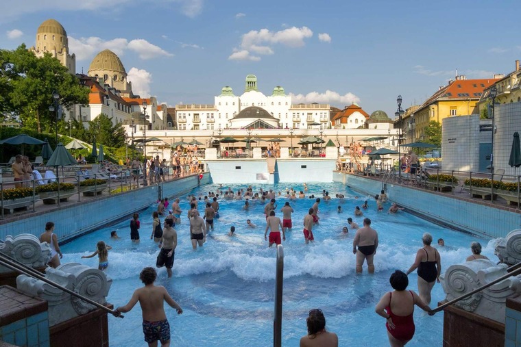 Budapest Thermen: Blick auf den schönen Außenbereich des Gellért-Thermalbads bei Tag. Viele Besucher:innen sind und gehen gerade in den Pool. 