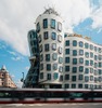 Prag Sehenswürdigkeiten: Blick auf das Tanzende Haus in Prag, davor sieht man eine Straßenbahn, die vorbei fährt. 
