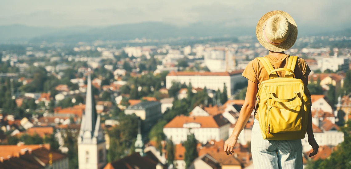 Städtetrips Europa: Eine junge Frau mit Rucksack blickt vom Schloss Ljubljana auf die Stadt hinab. 