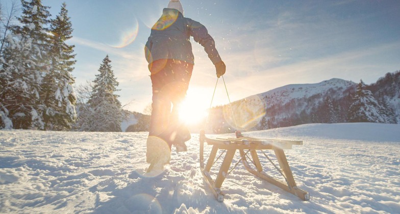 Eine Person zieht in einer schneebedeckten Landschaft einen Schlitten hinter sich her